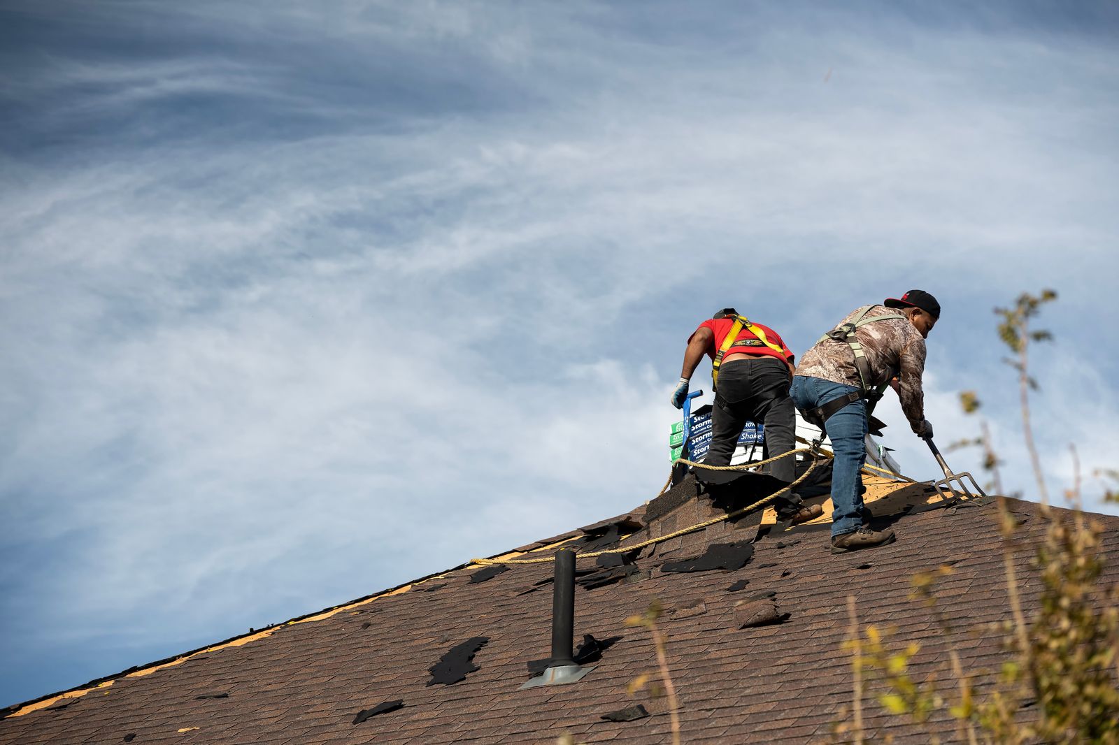 Two roofers on a steep pitched roof tearing off old shingles after storm damage